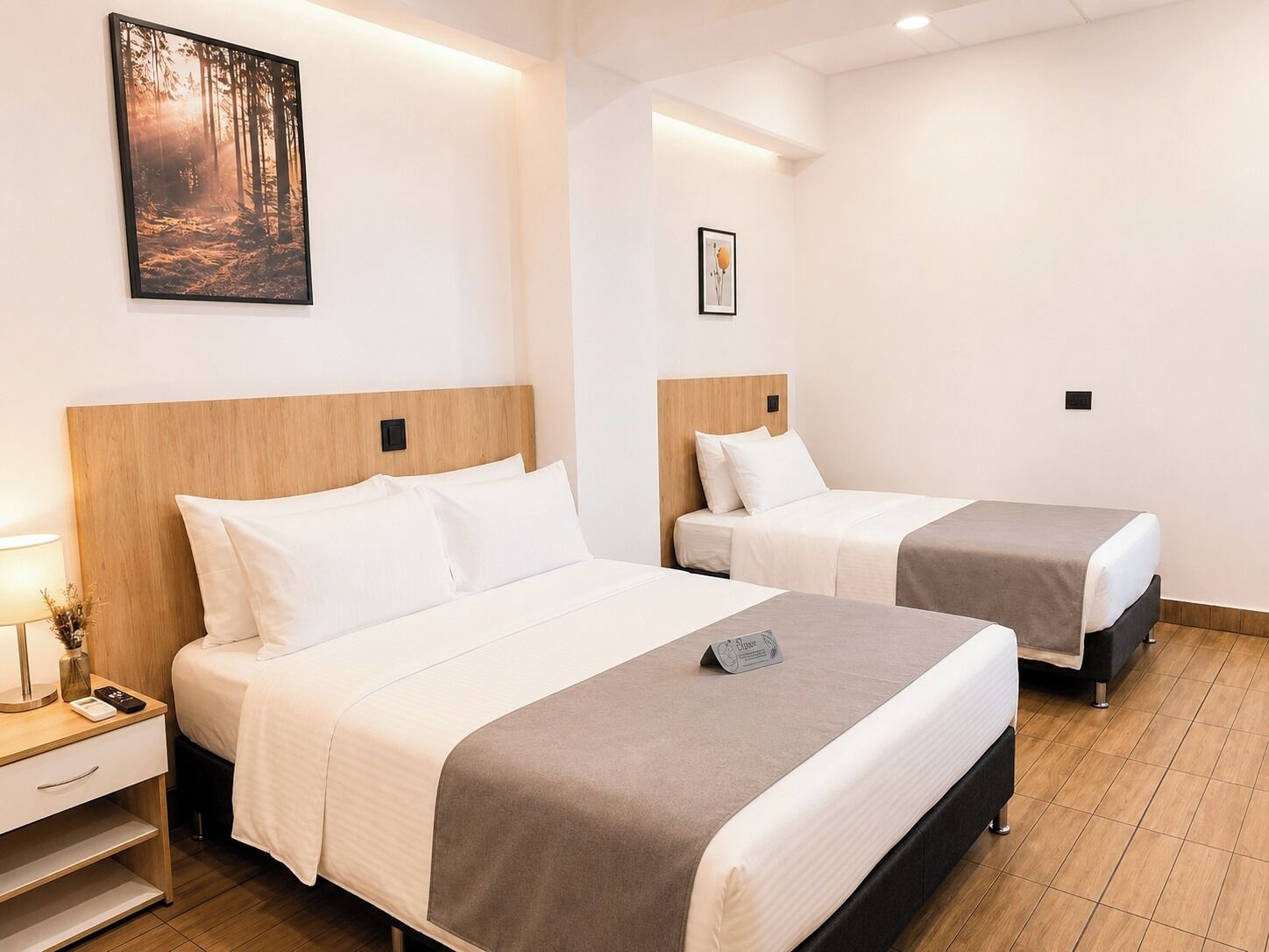 Ein Hotelzimmer mit zwei Betten, einem Nachttisch mit Lampe und einem gerahmten Bild an der Wand.
