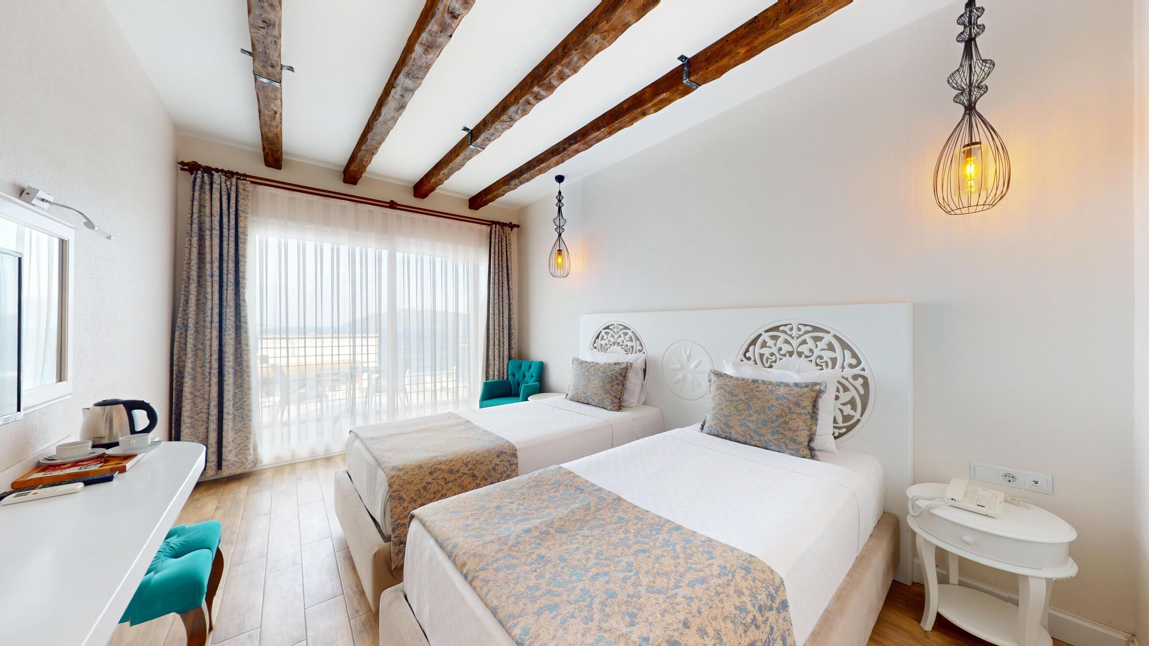 A hotel room with two beds, a desk with a kettle, and a view of the beach.