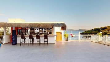 Eine Bar mit Reetdach, Sitzgelegenheiten und Meerblick.