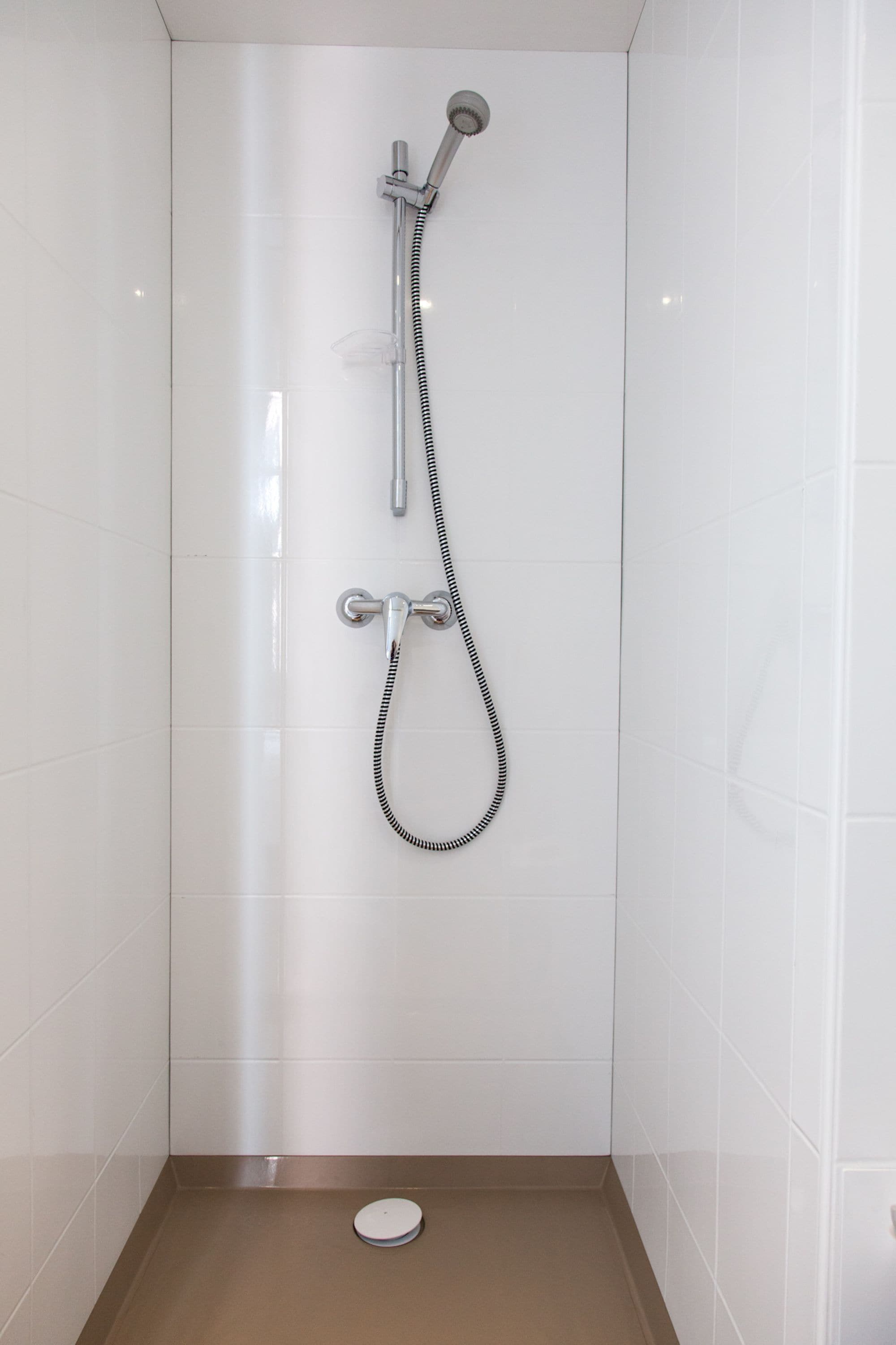 A small, enclosed shower area with a handheld showerhead and a fixed showerhead on a wall.