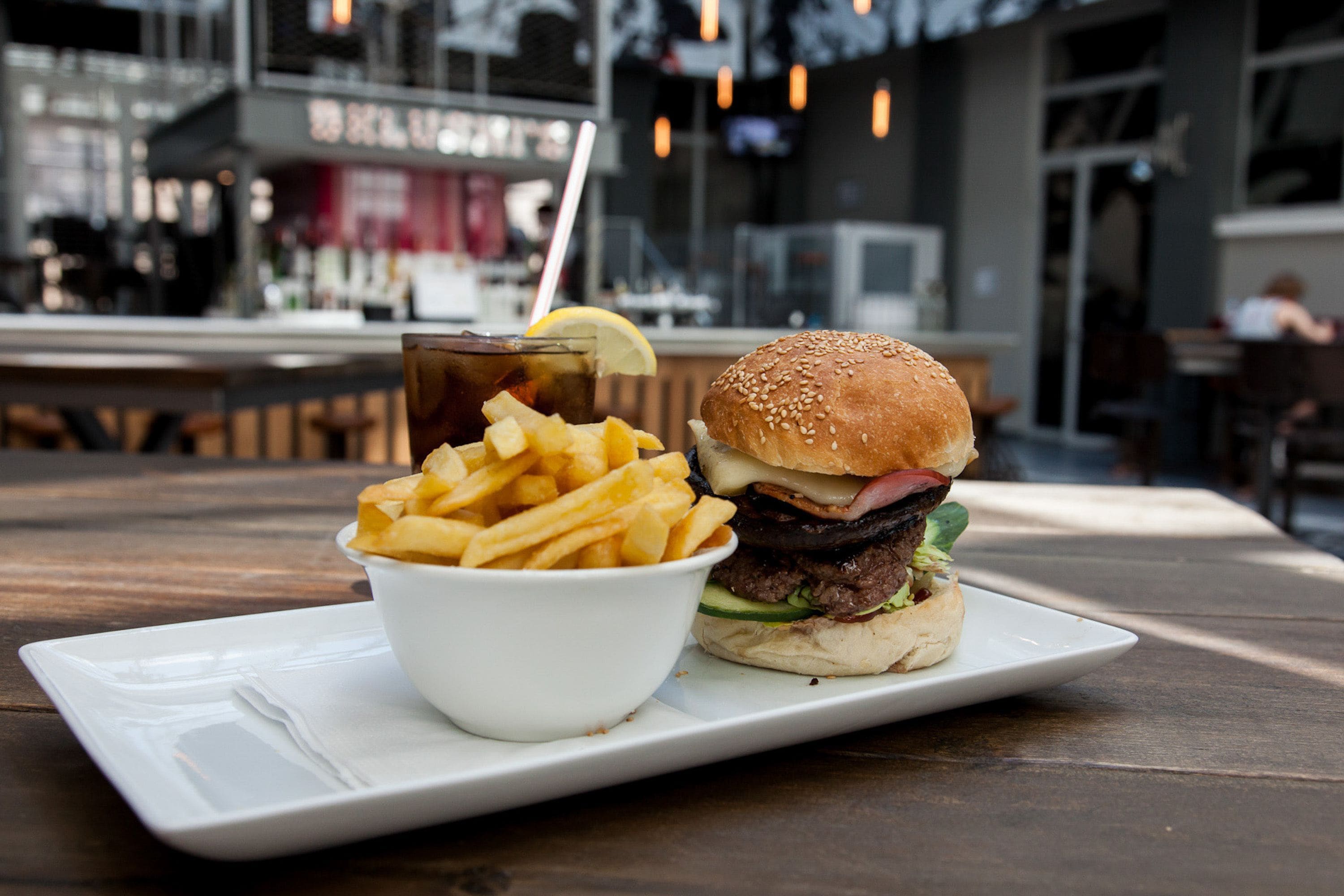 A burger and fries on a white plate, with a drink in the background.