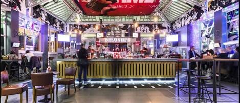 Un bar intérieur avec un plafond haut, des néons et un comptoir central.