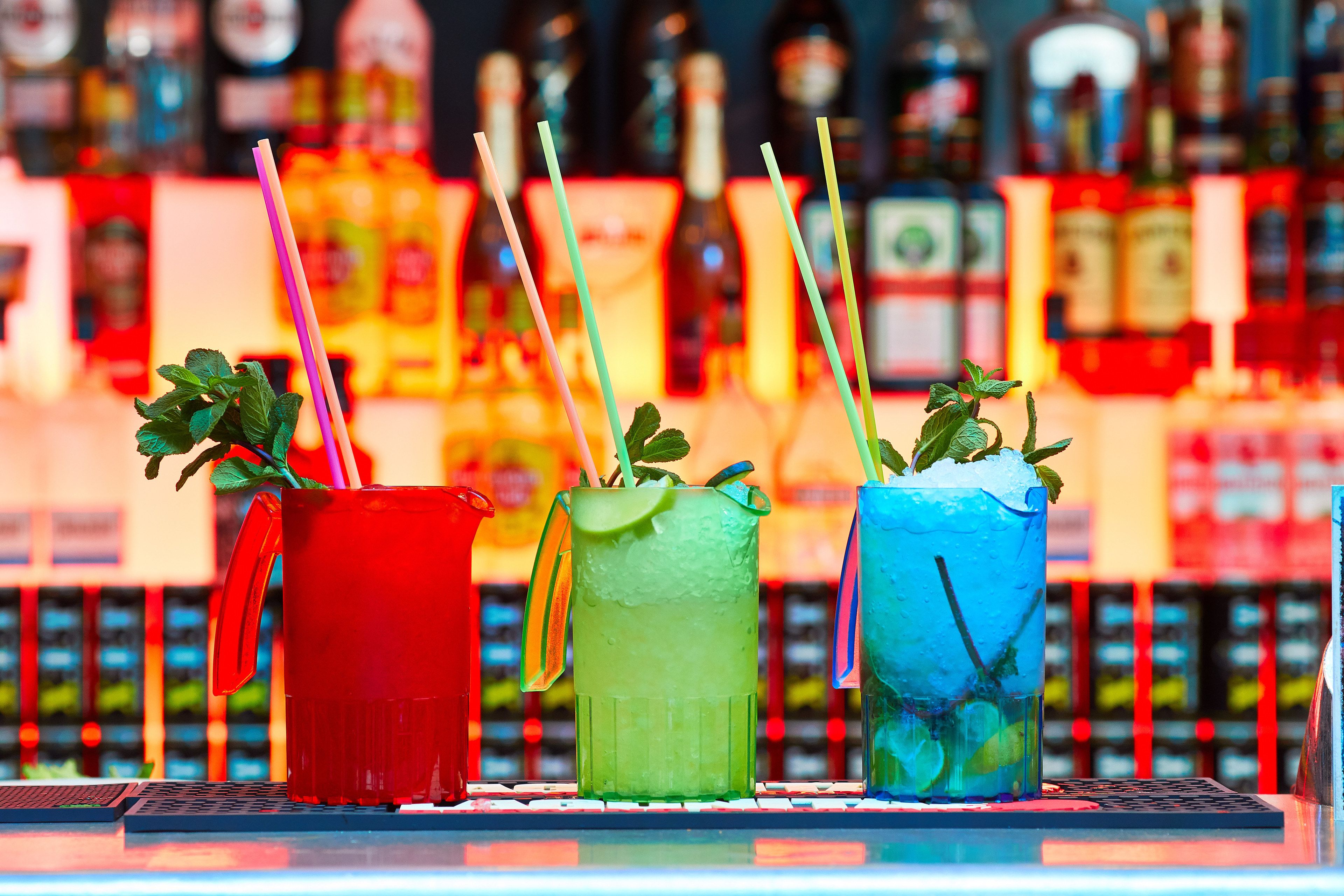 Tre färgglada drinkar med sugrör och myntablad på en bardisk.