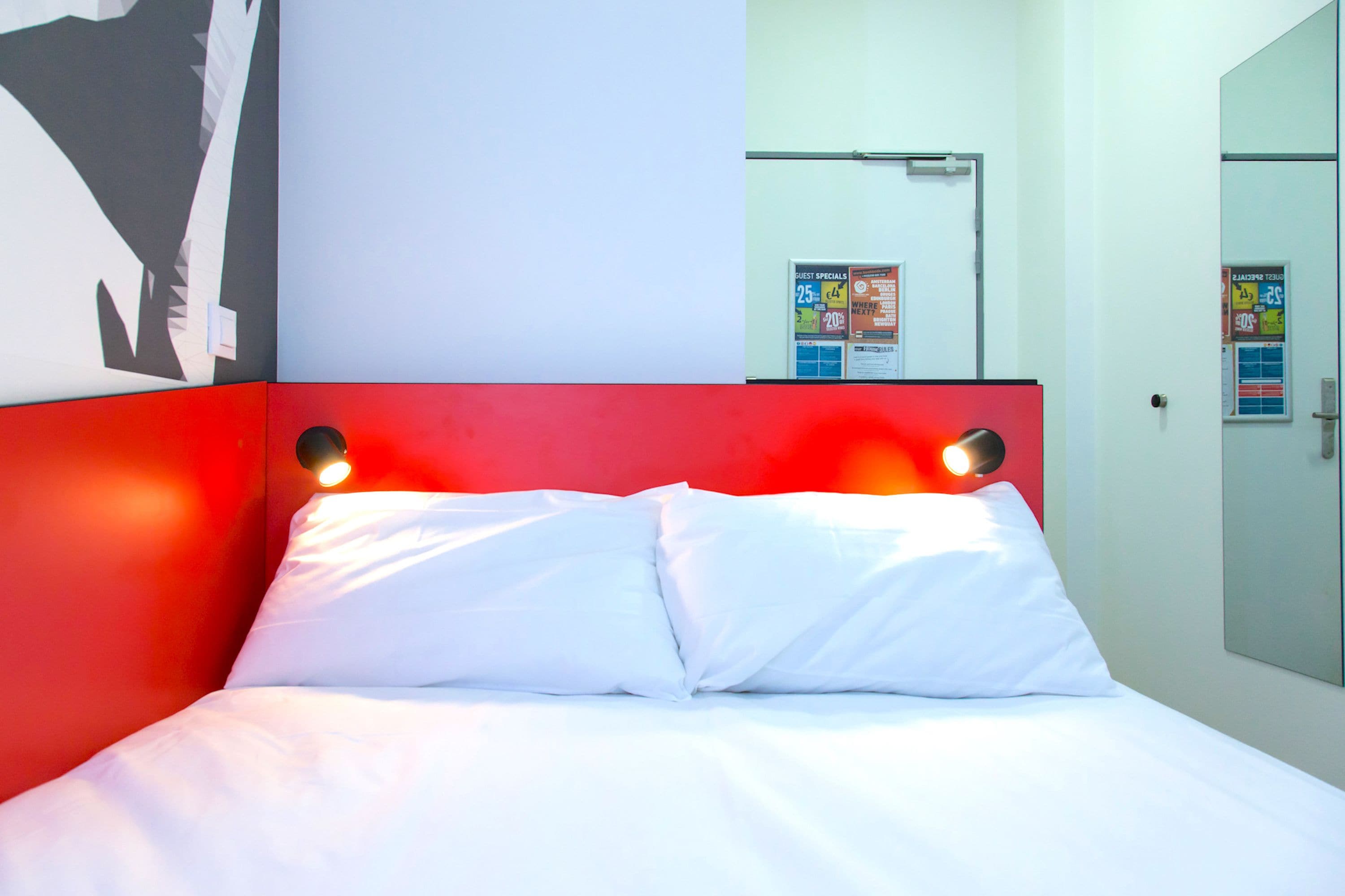 A modern hotel room with a red accent wall, a large bed with white linens, and a wall-mounted TV.