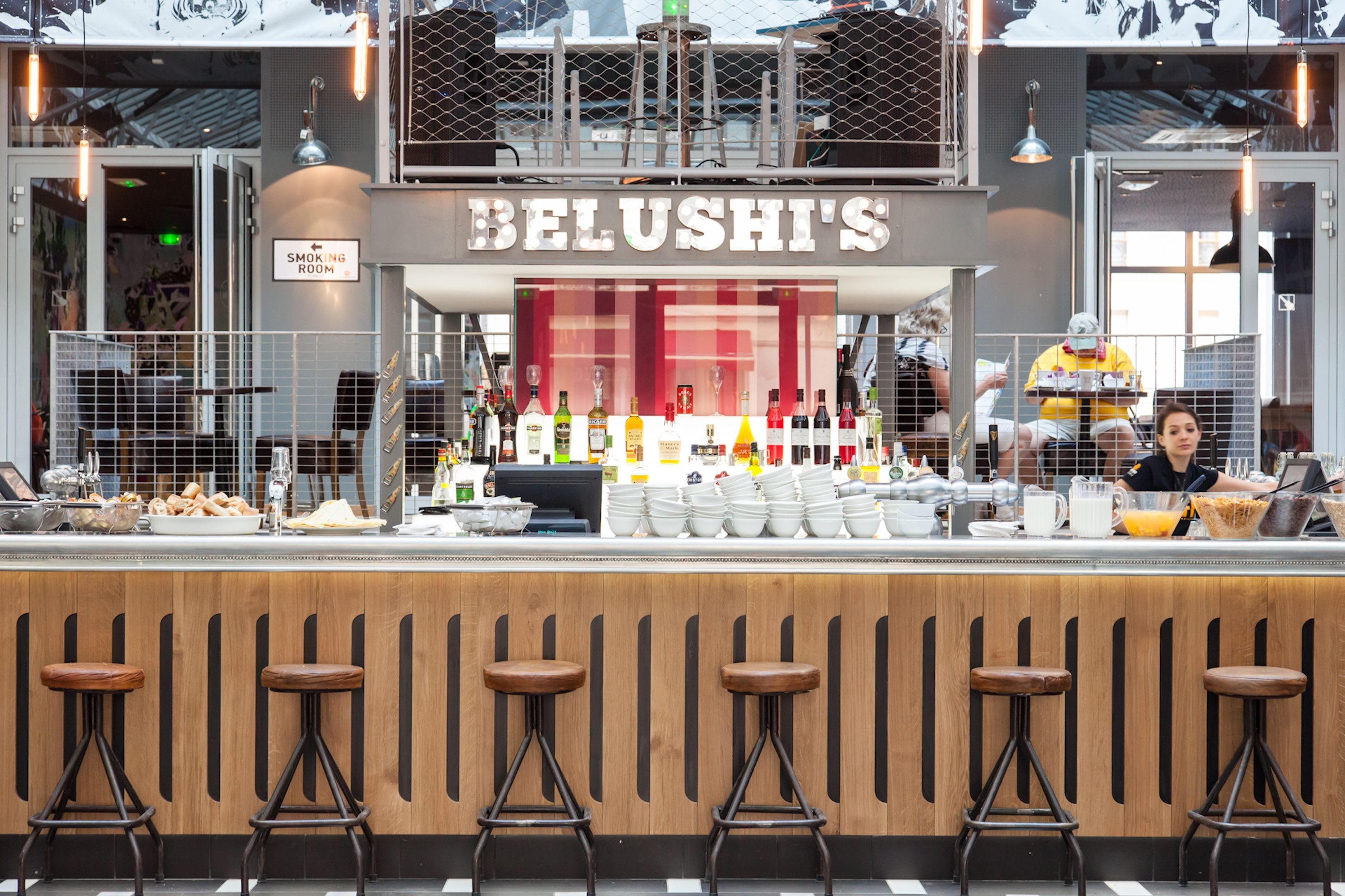 A bar area with stools, a counter with bottles, and a sign reading "BELUSH'S".