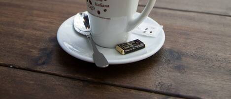 A cup of coffee on a wooden table with a spoon and a small packet, in a cafe with a blurred background.