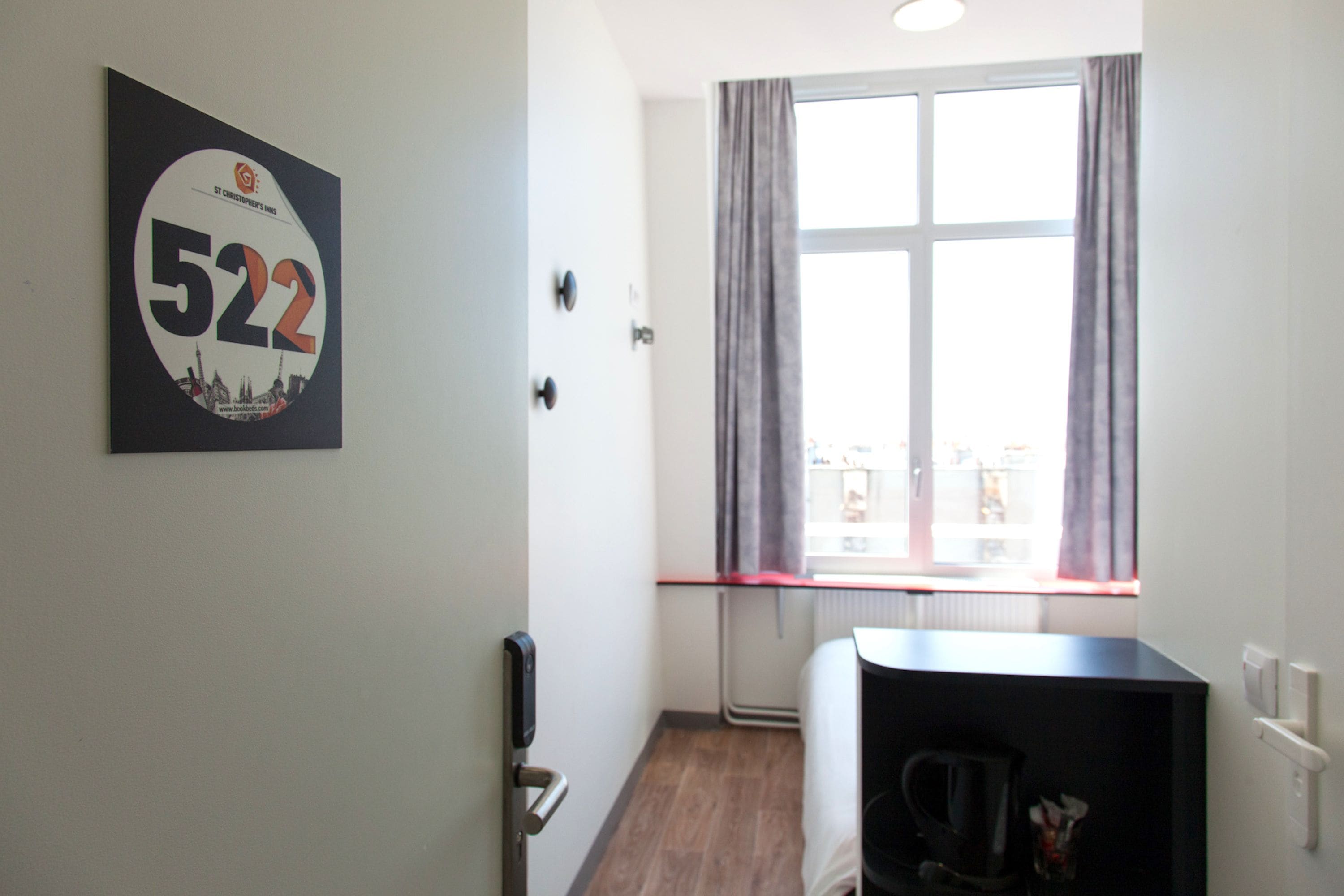 A hotel room with a large window, a door with a handle, and a wall-mounted number sign.