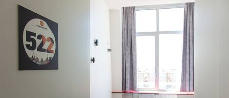 Una habitación de hotel con un ventanal grande, una puerta con manija y un cartel con número adherido a la pared.