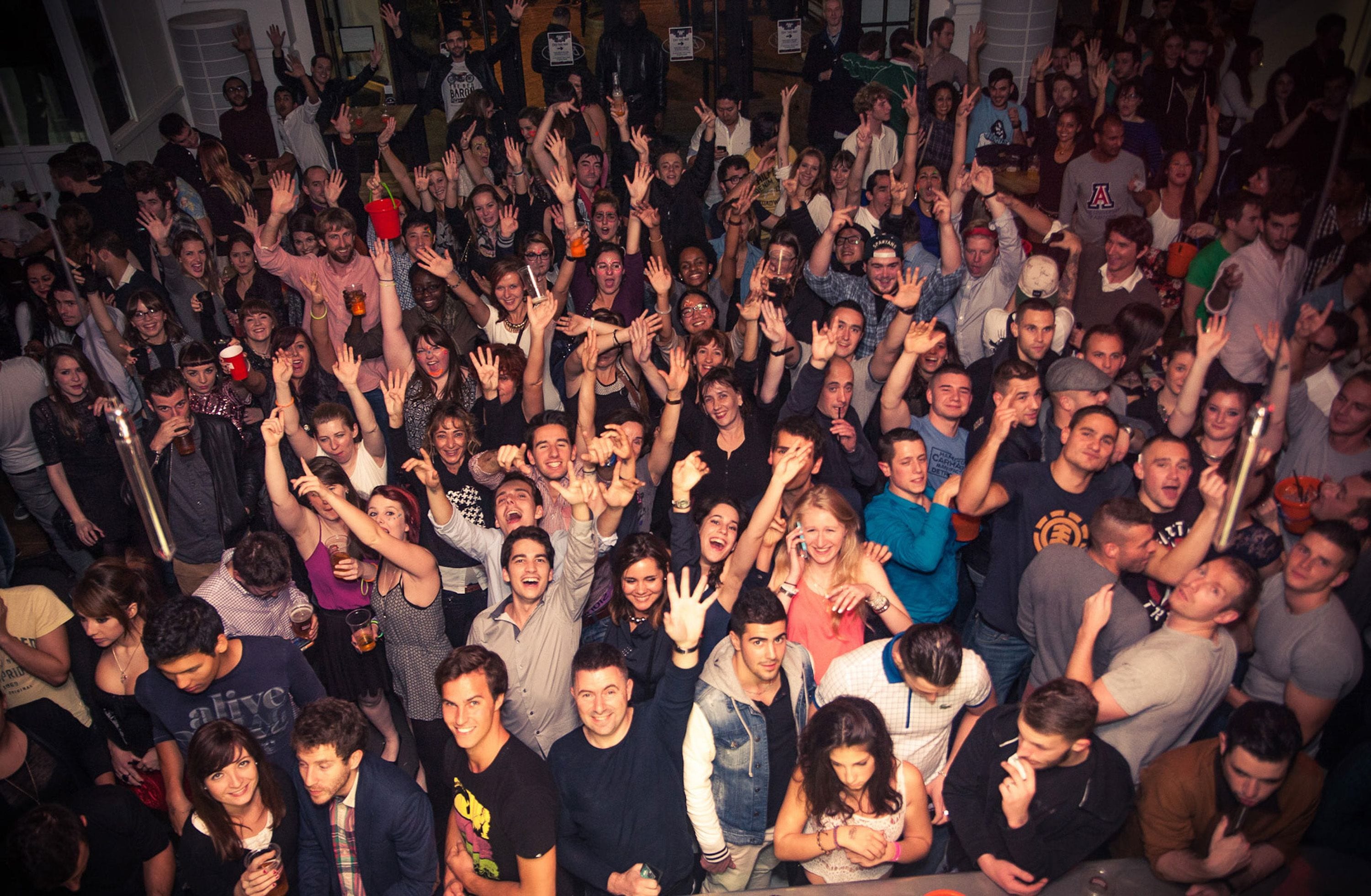 A crowded indoor event with people standing and raising their hands.