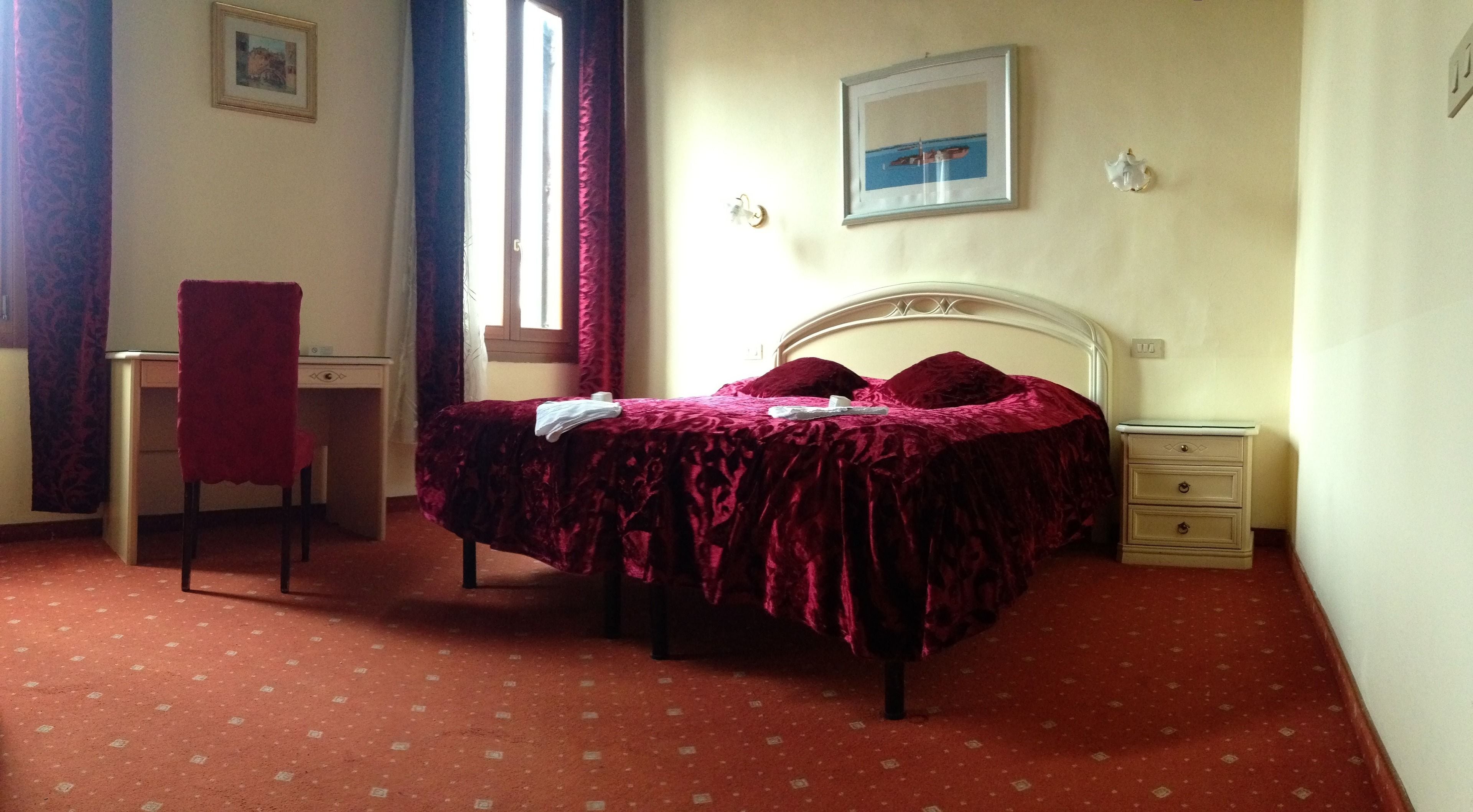 A bedroom with a bed, a desk, a chair, a nightstand, and a window.