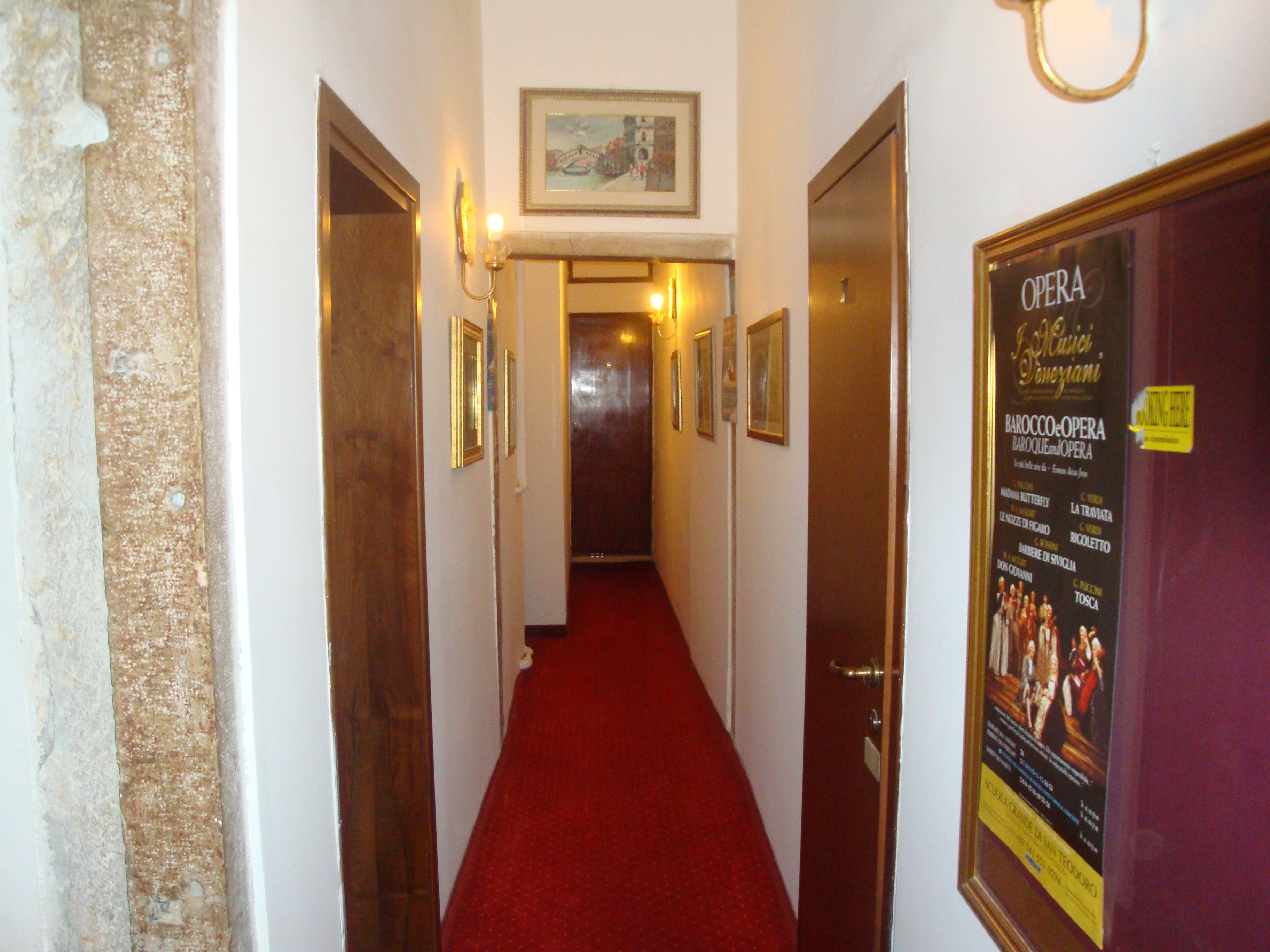 Een gang met ingelijste foto’s aan de muur, een rood tapijt en een deur met een poster voor een opera-evenement.