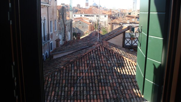 Vista desde una ventana que da a un paisaje urbano con edificios tradicionales y una imponente torre de reloj.