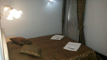 Un dormitorio con una colcha estampada, una almohada, una lámpara de noche y una ventana con cortinas.
