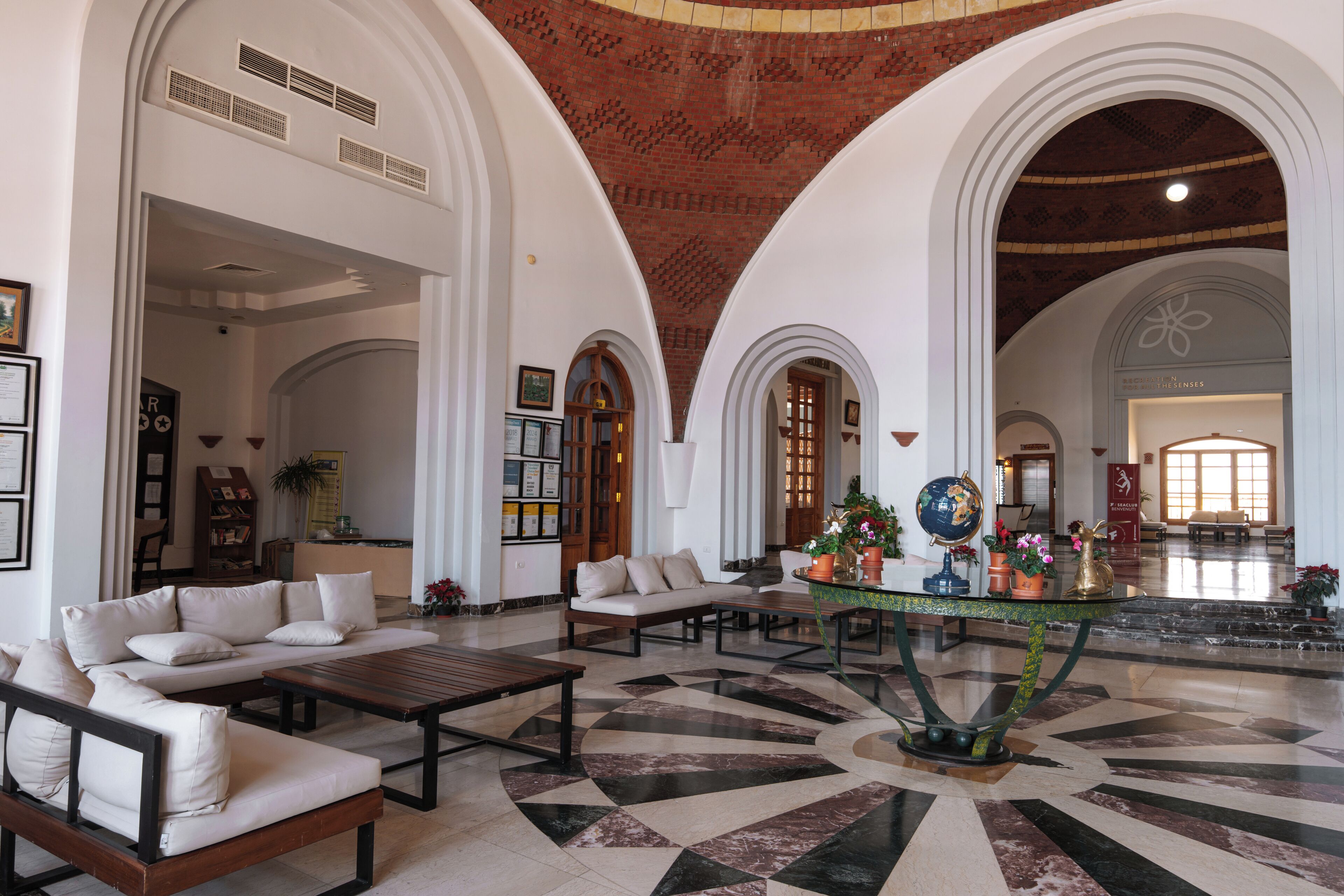 Eine großzügige Lobby mit hohen Decken, Rundbogenöffnungen und einem zentralen Couchtisch, umgeben von Sofas und Sesseln.