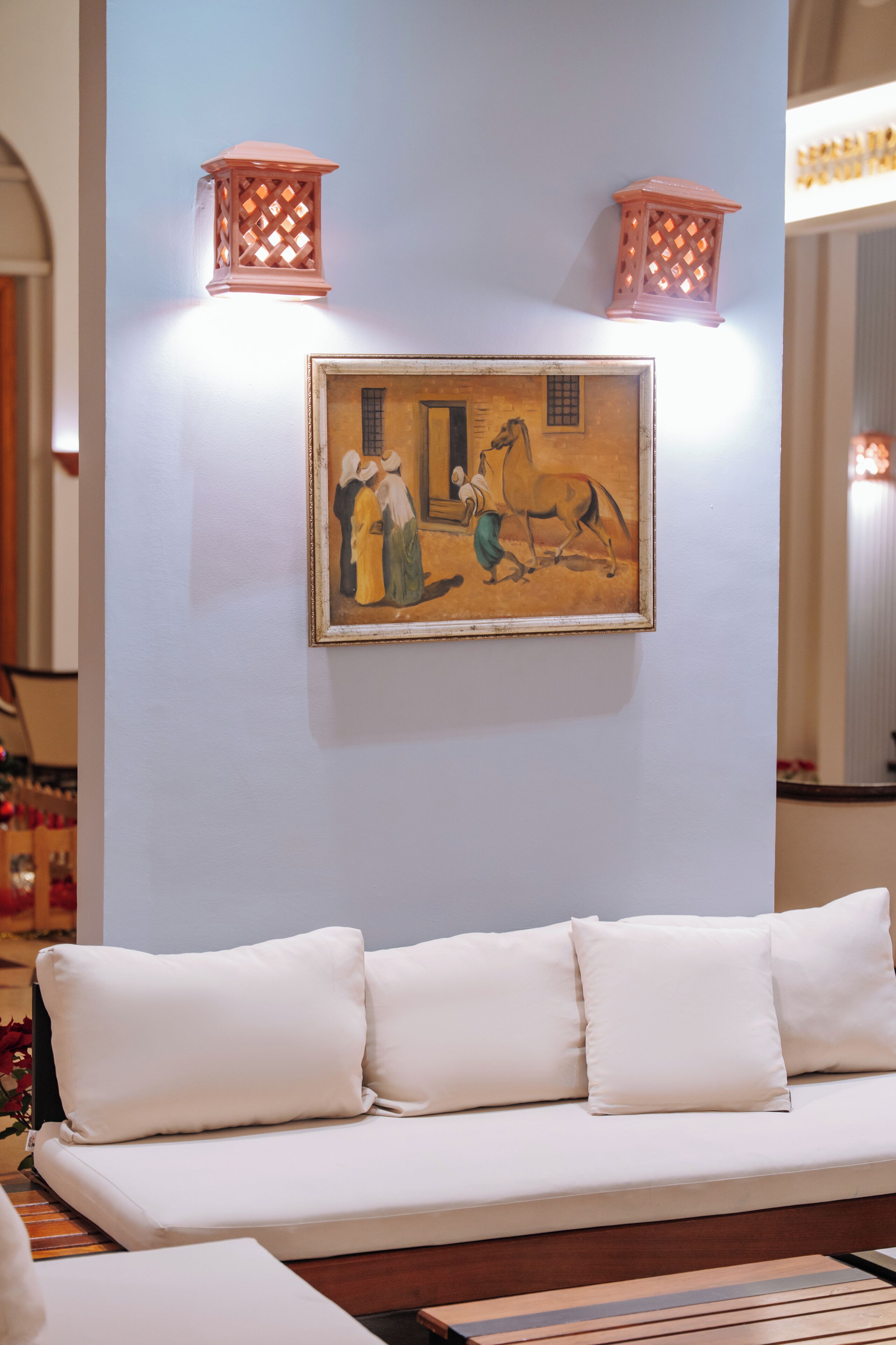 A room with a white sofa, a framed painting, and two wall-mounted lanterns.