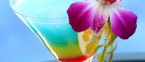 Ein Martini-Glas mit einem schichtartigen Getränk und einer violetten Orchideenblüte auf einer spiegelnden Oberfläche.