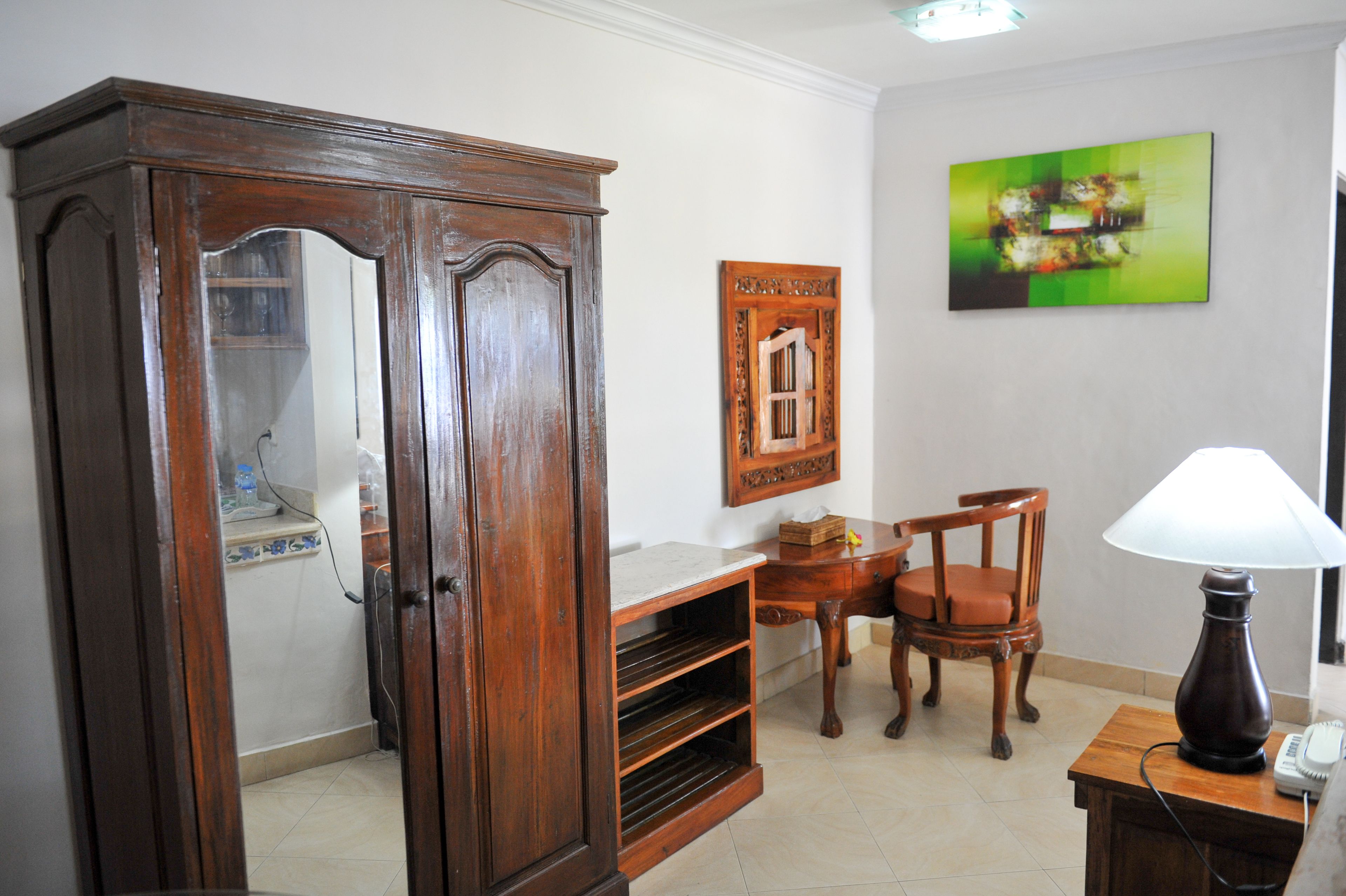 A room with a wooden cabinet, a chair, a desk with a lamp, and a framed picture on the wall.