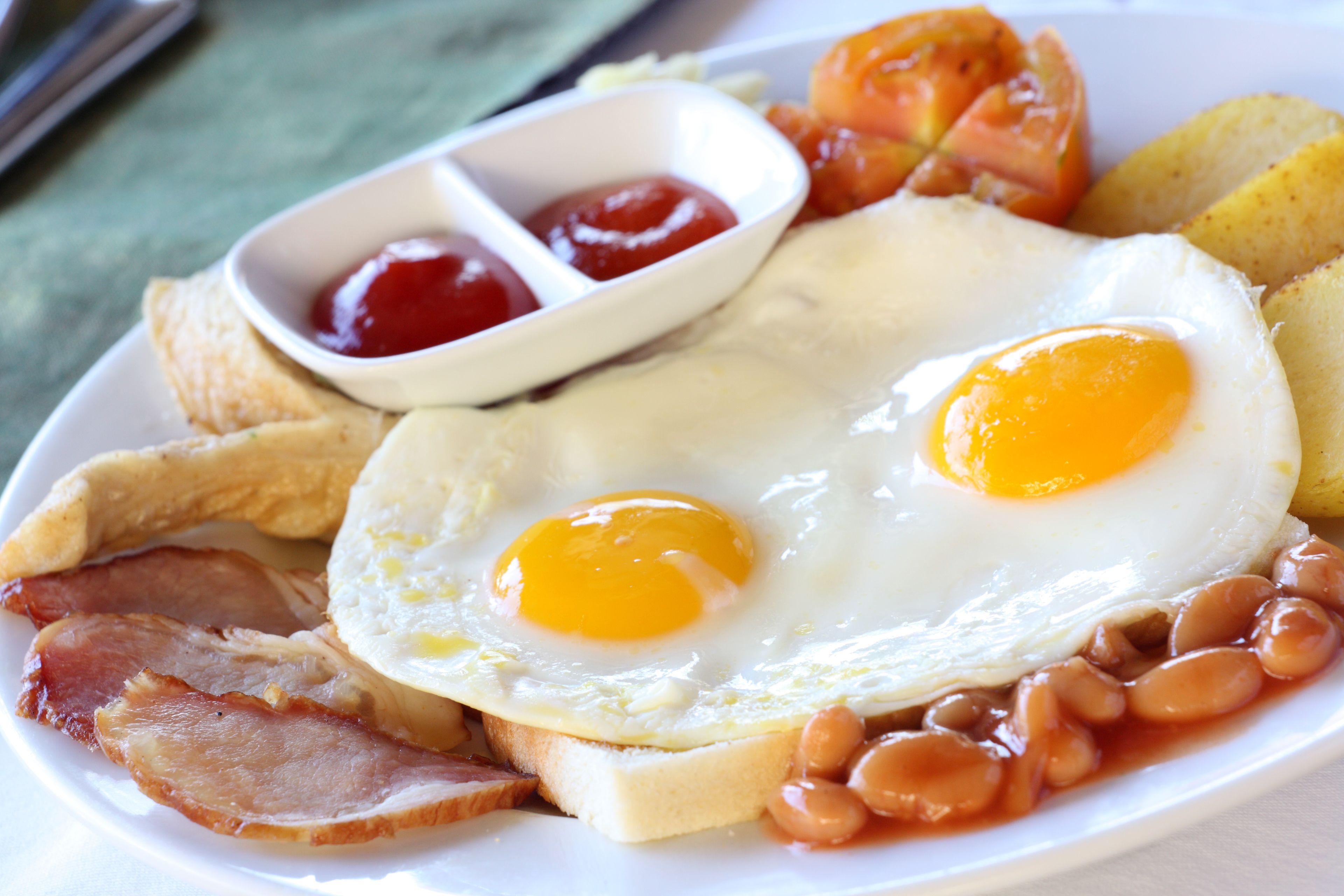 A plate of breakfast food including eggs, bacon, beans, toast, and tomatoes.