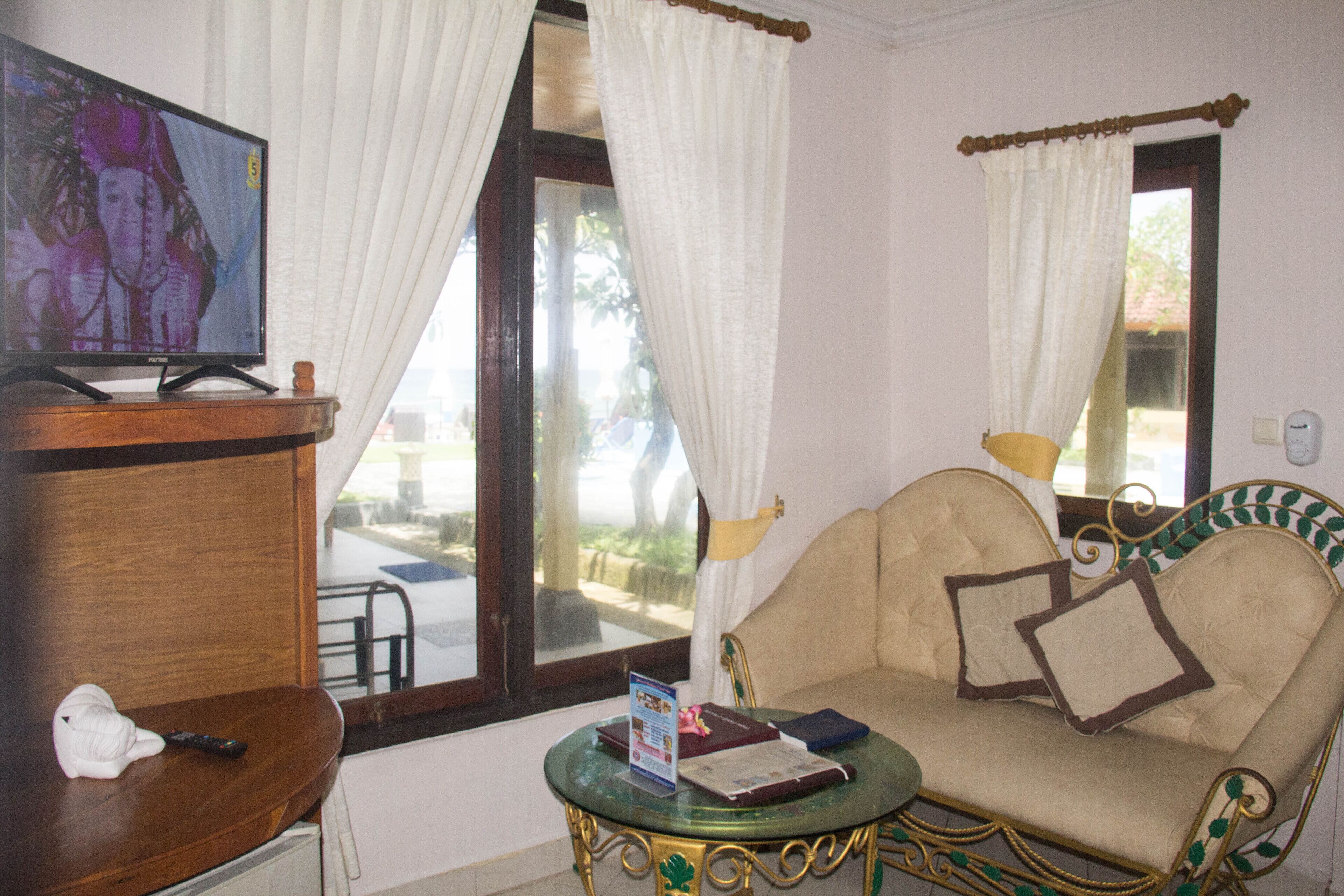 A room with a sofa, a small table, a television, and a window with curtains.