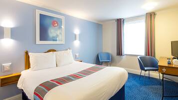A hotel room with a large bed, a desk, a chair, and a window with curtains.