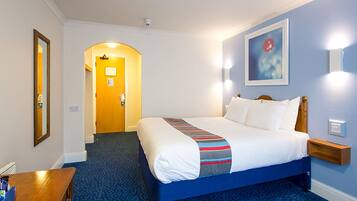 A hotel room with a bed, a desk, a chair, a mirror, a door, and a wall-mounted light fixture.
