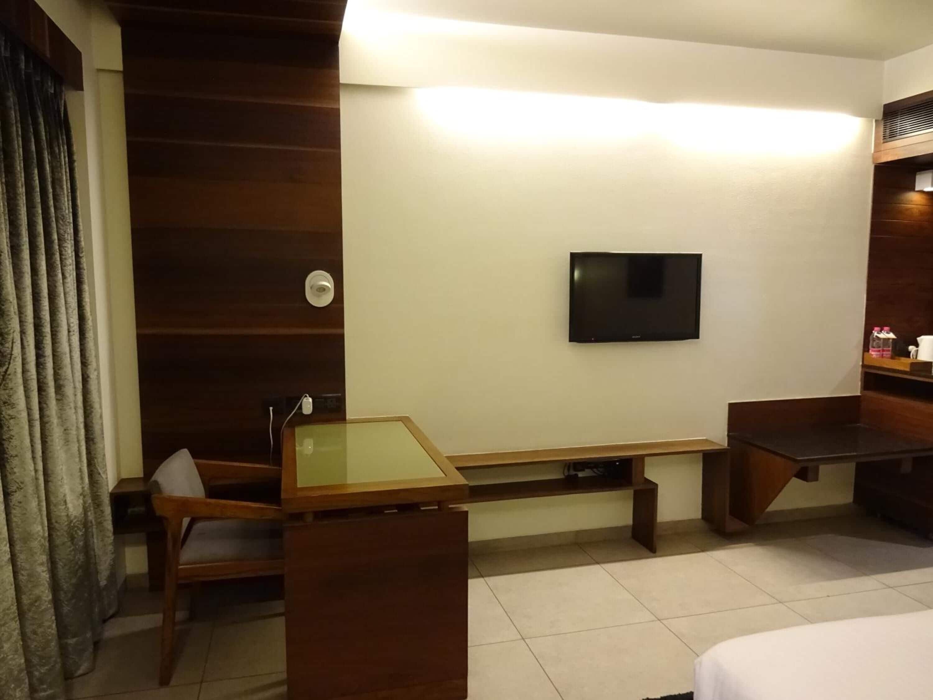 Habitación de hotel con un escritorio de madera, una silla, un televisor montado en la pared y una cama.