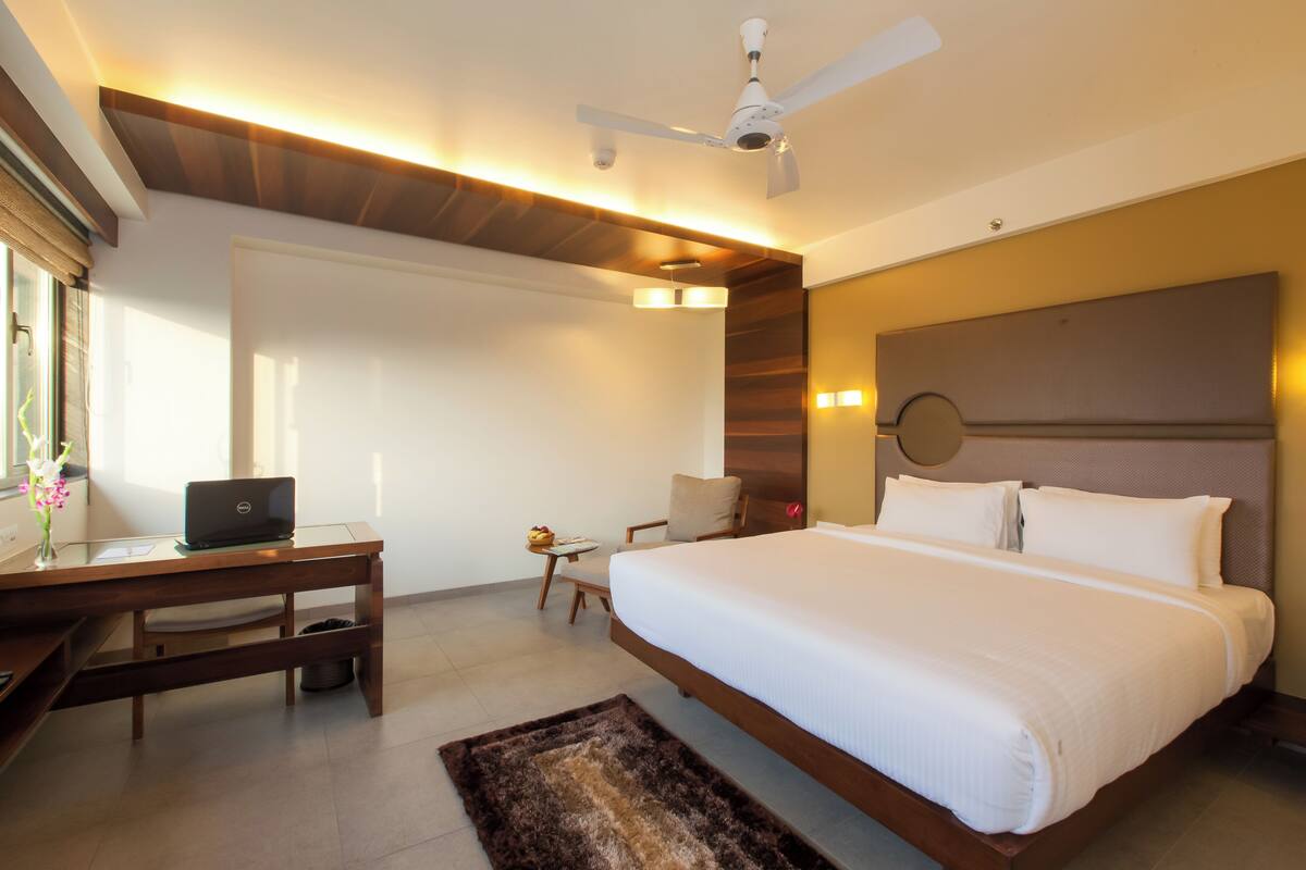 Een moderne hotelkamer met een groot bed, een bureau met een laptop, een tafeltje en een plafondventilator.