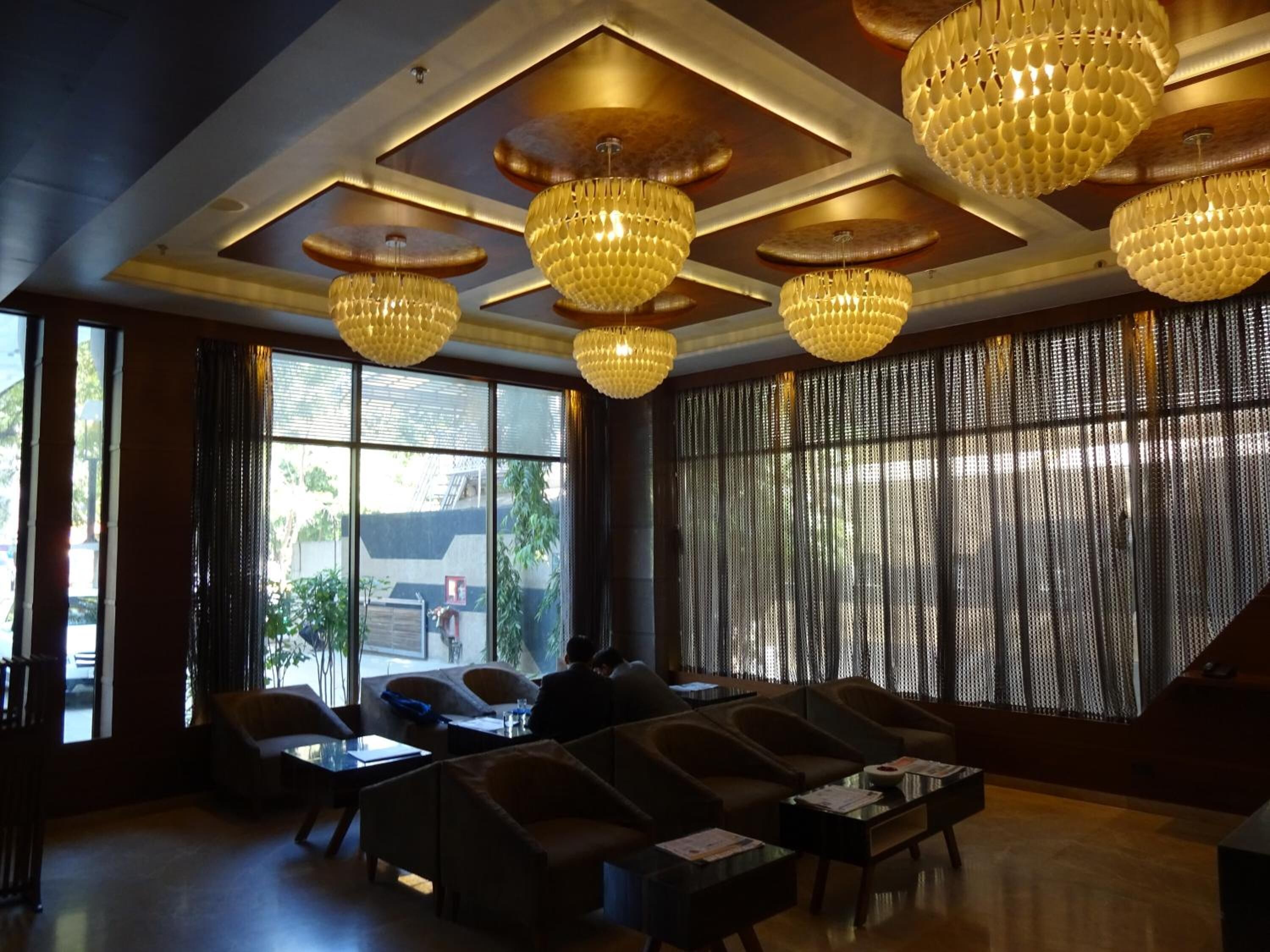 Un vestíbulo moderno con ventanas amplias, una zona de estar con sofás y sillones, y varios candelabros.