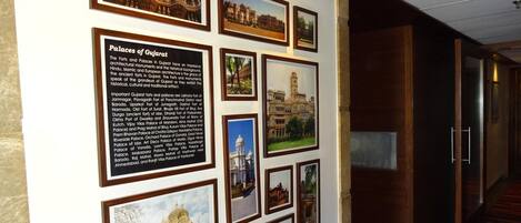 A hallway with framed pictures of various buildings and a sign about the Palaces of Gujarat.