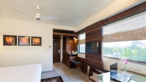 Une chambre d’hôtel avec un lit, un bureau avec un ordinateur portable, une télévision et des œuvres d’art accrochées au mur.