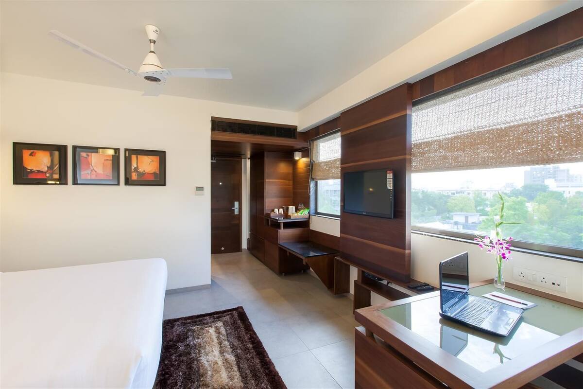Een hotelkamer met een bed, een bureau met een laptop, een televisie en kunst aan de muur.