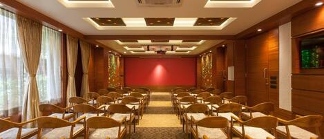 A conference room with rows of wooden chairs, a red screen, and a ceiling with recessed lighting.