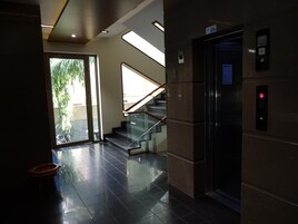 Un interior moderno con una escalera de cristal, un ascensor y una puerta que da a un espacio luminoso con luz natural.