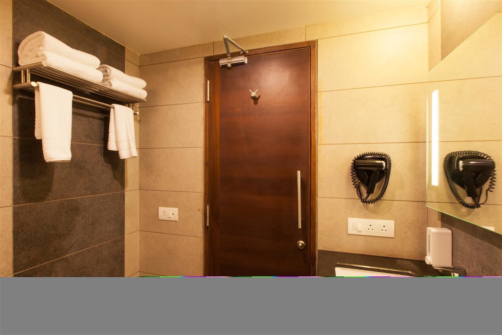 A bathroom with a wooden door, a towel rack with folded towels, and a hairdryer mounted on the wall.