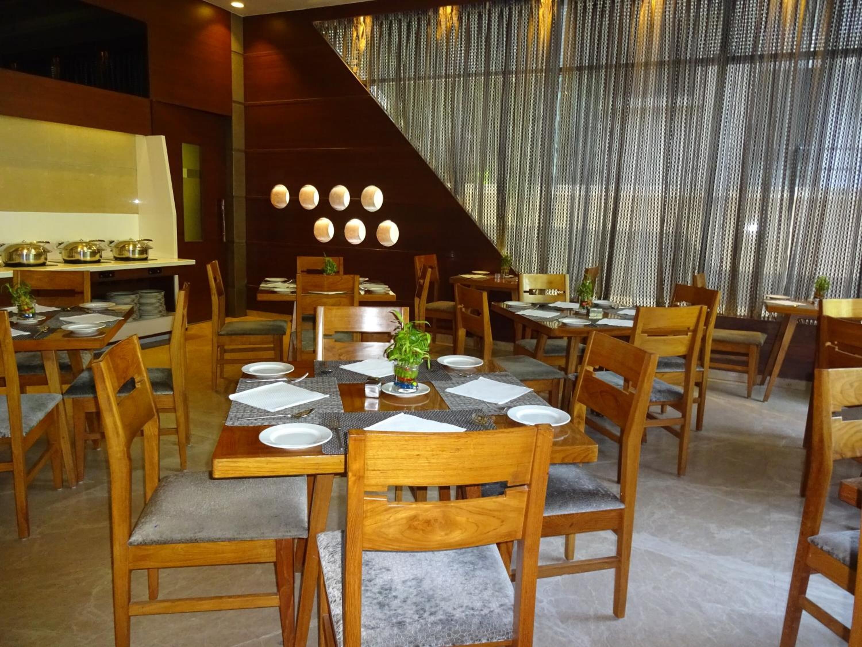 Un restaurante con mesas y sillas de madera, un ventanal con cortinas y una escalera.