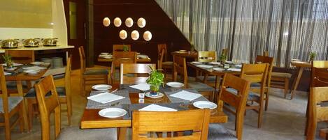 Un restaurante con mesas y sillas de madera, un ventanal con cortinas y una escalera.