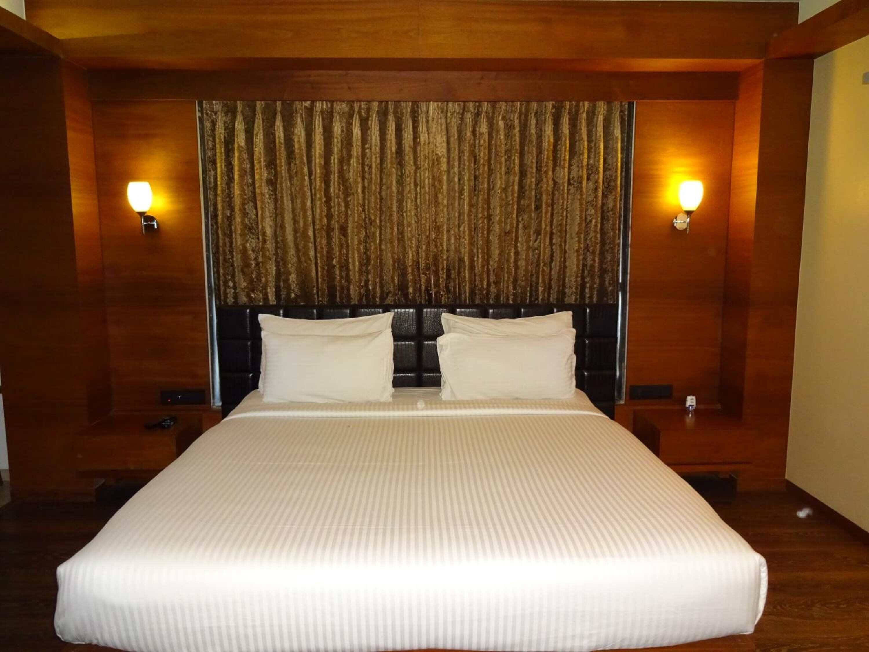 A large bed with a headboard, two bedside lamps, and a curtain.