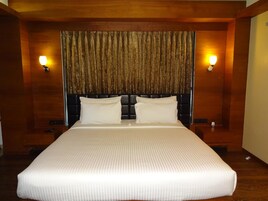 A large bed with a headboard, two bedside lamps, and a curtain.