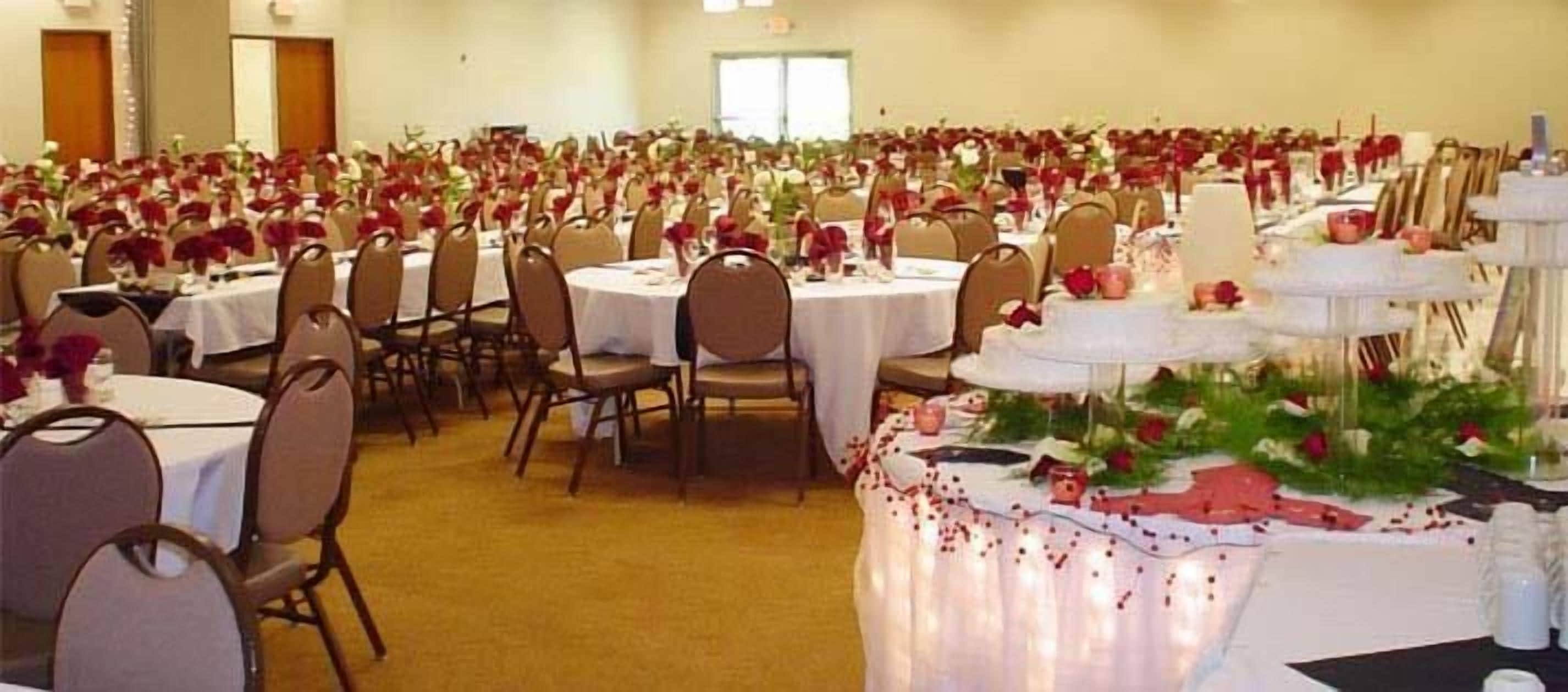 A banquet hall with round tables, chairs, and a tiered cake centerpiece.