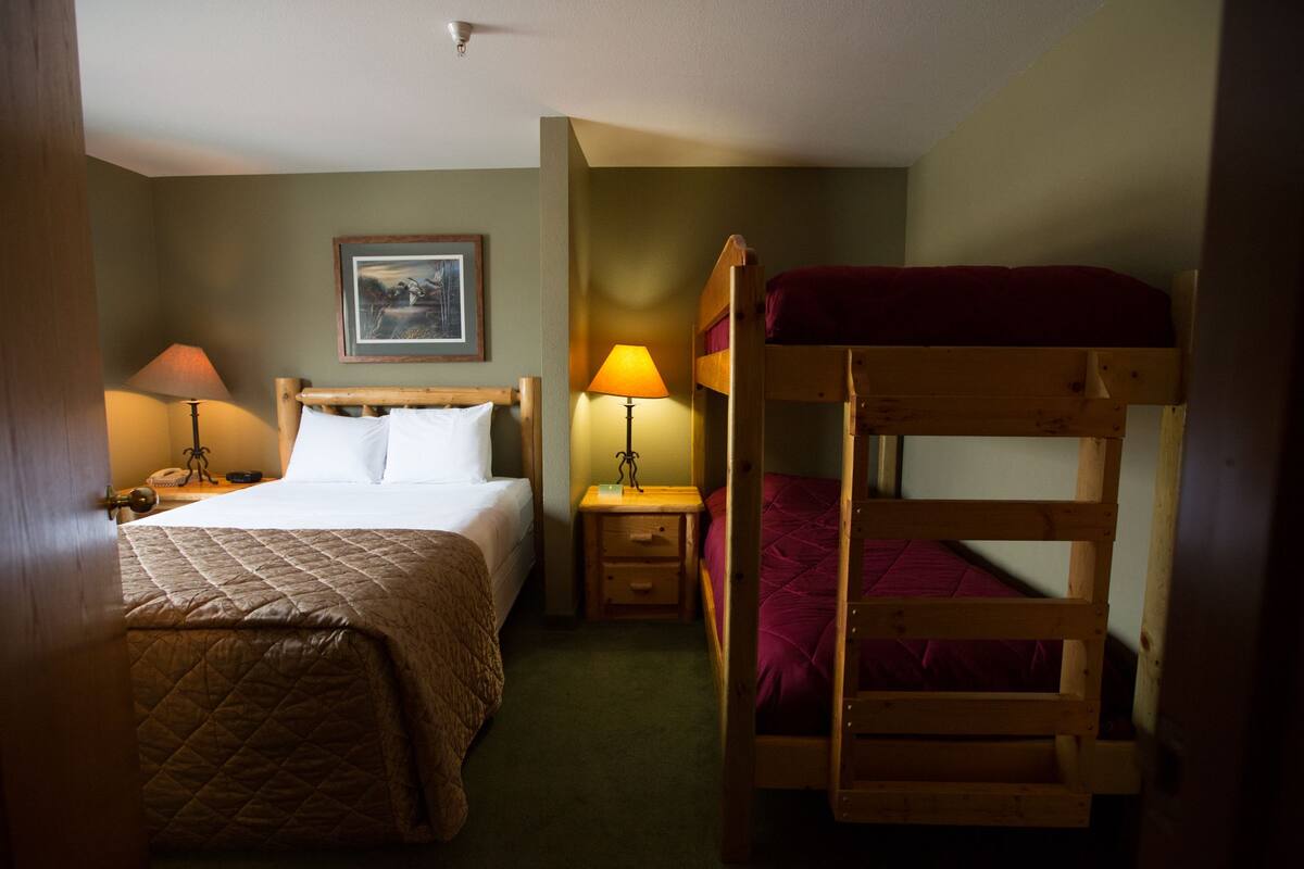 Een kamer met een enkel bed, nachtkastje met lamp, een stapelbed en een ingelijst schilderij aan de muur.