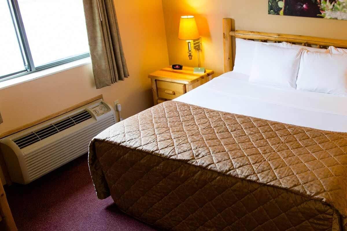 Een hotelkamer met een bed, twee nachtkastjes met lampen, een heater en een raam met gordijnen.