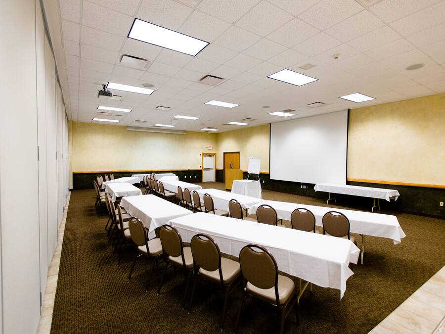 A conference room with long tables and chairs, a projector screen, and a carpeted floor.