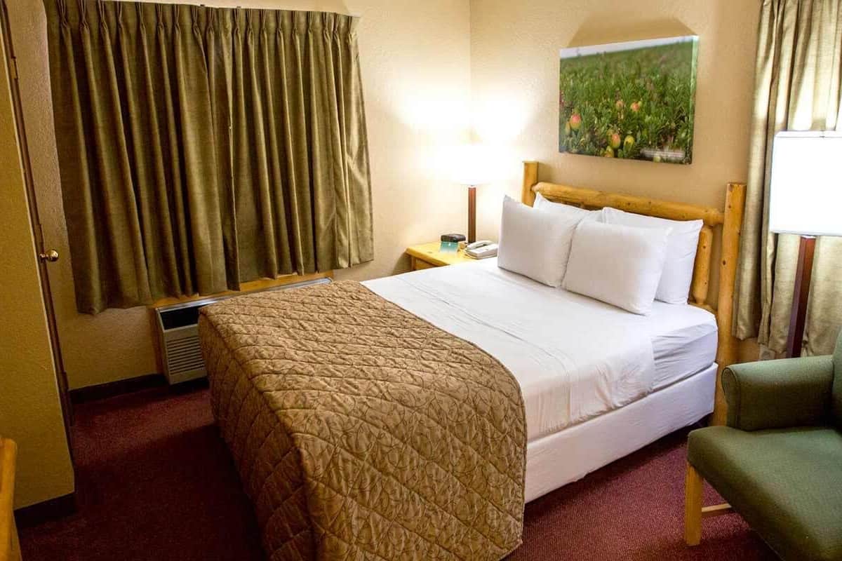 Een hotelkamer met een bed, een stoel, een nachtkastje, een lamp en een schilderij aan de muur.