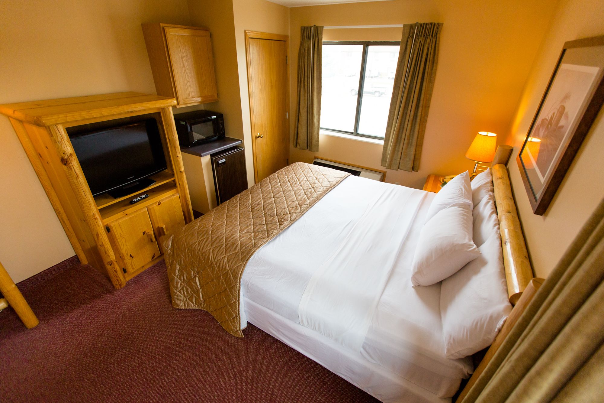 Una habitación de hotel con cama, televisor, una kitchenette pequeña y ventana con cortinas.