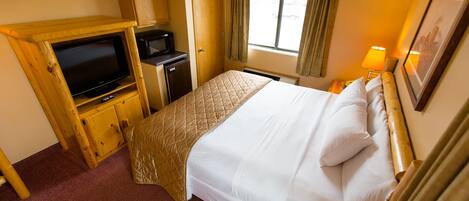Una habitación de hotel con cama, televisor, una kitchenette pequeña y ventana con cortinas.