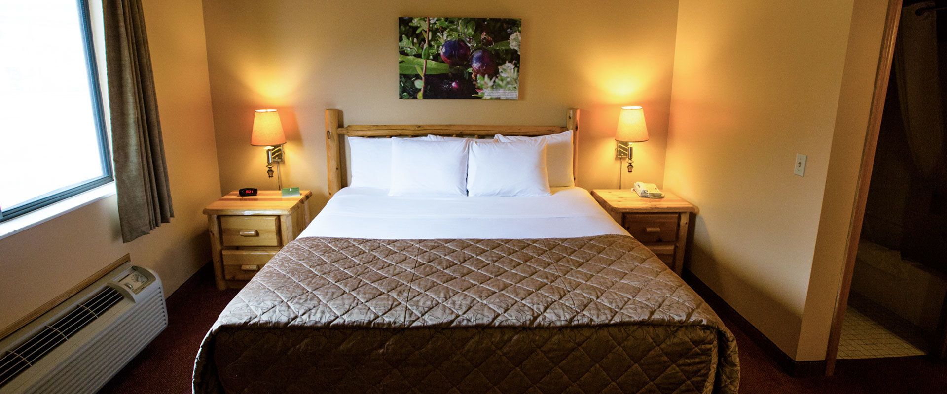 A hotel room with a bed, two bedside tables with lamps, a wall-mounted picture, and a window with curtains.
