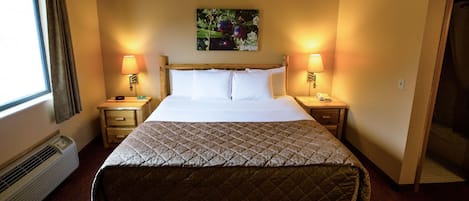 A hotel room with a bed, two bedside tables with lamps, a wall-mounted picture, and a window with curtains.