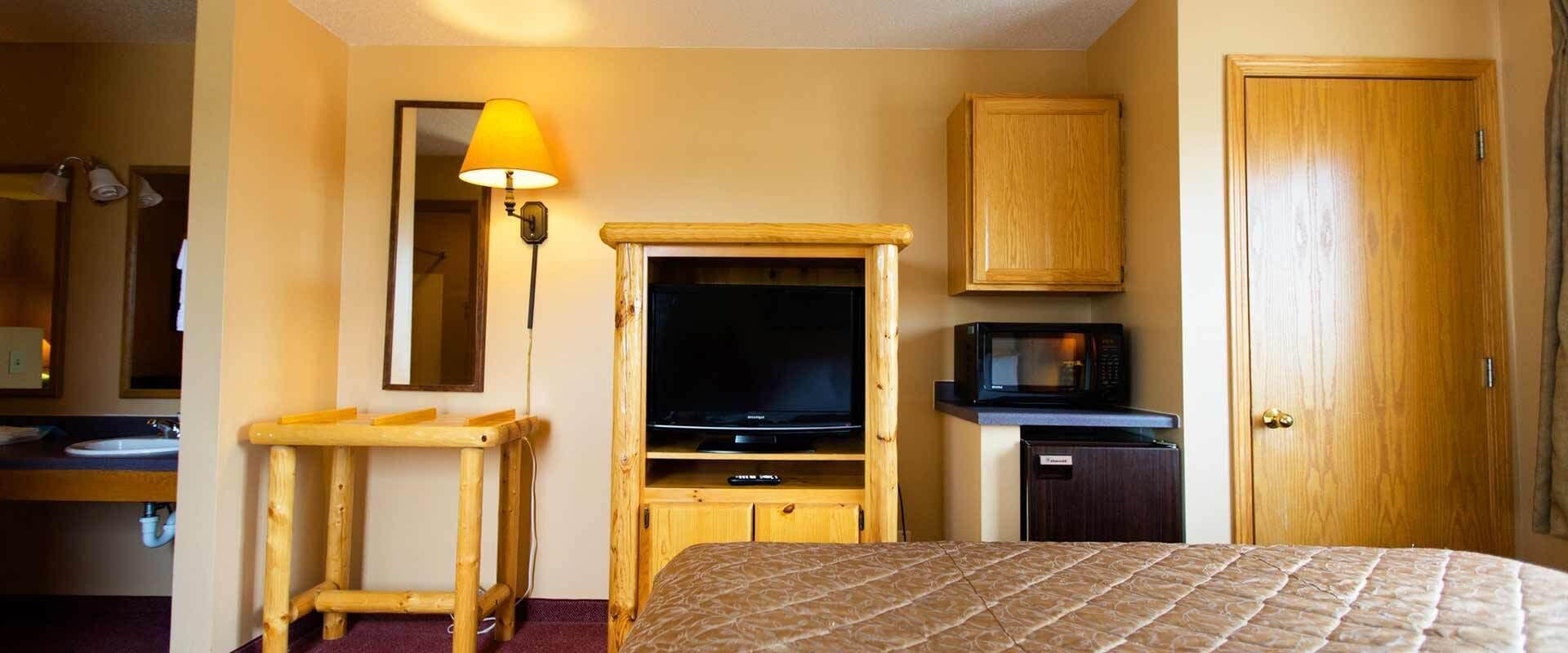 Habitación de hotel con cama, escritorio de madera, televisor, microondas, mueble y puerta.