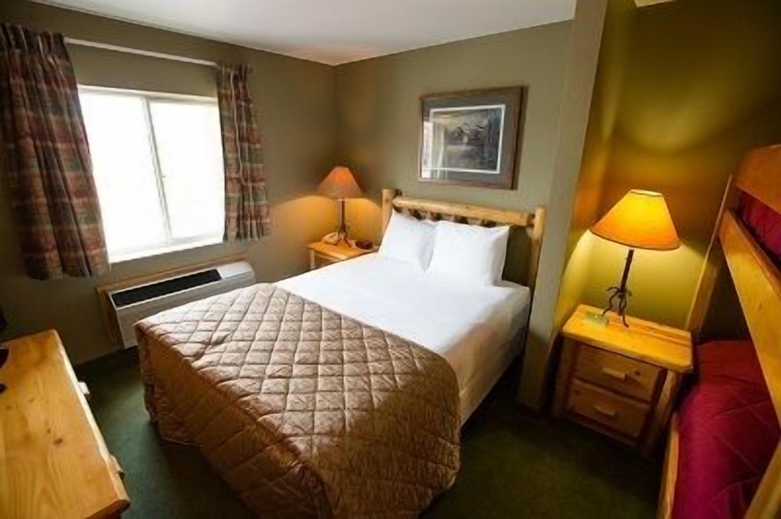 A hotel room with a bed, two bedside tables with lamps, a window with curtains, and a framed picture on the wall.