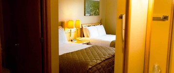Una habitación de hotel con dos camas, una mesita de noche con lámparas y un cuadro en la pared.